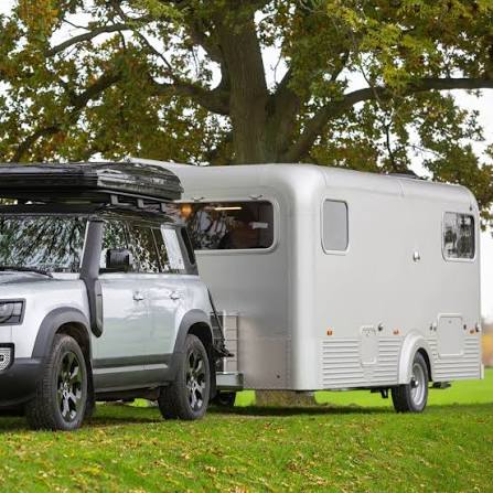 Terreinwagen met aangekoppelde caravan onder een grote boom